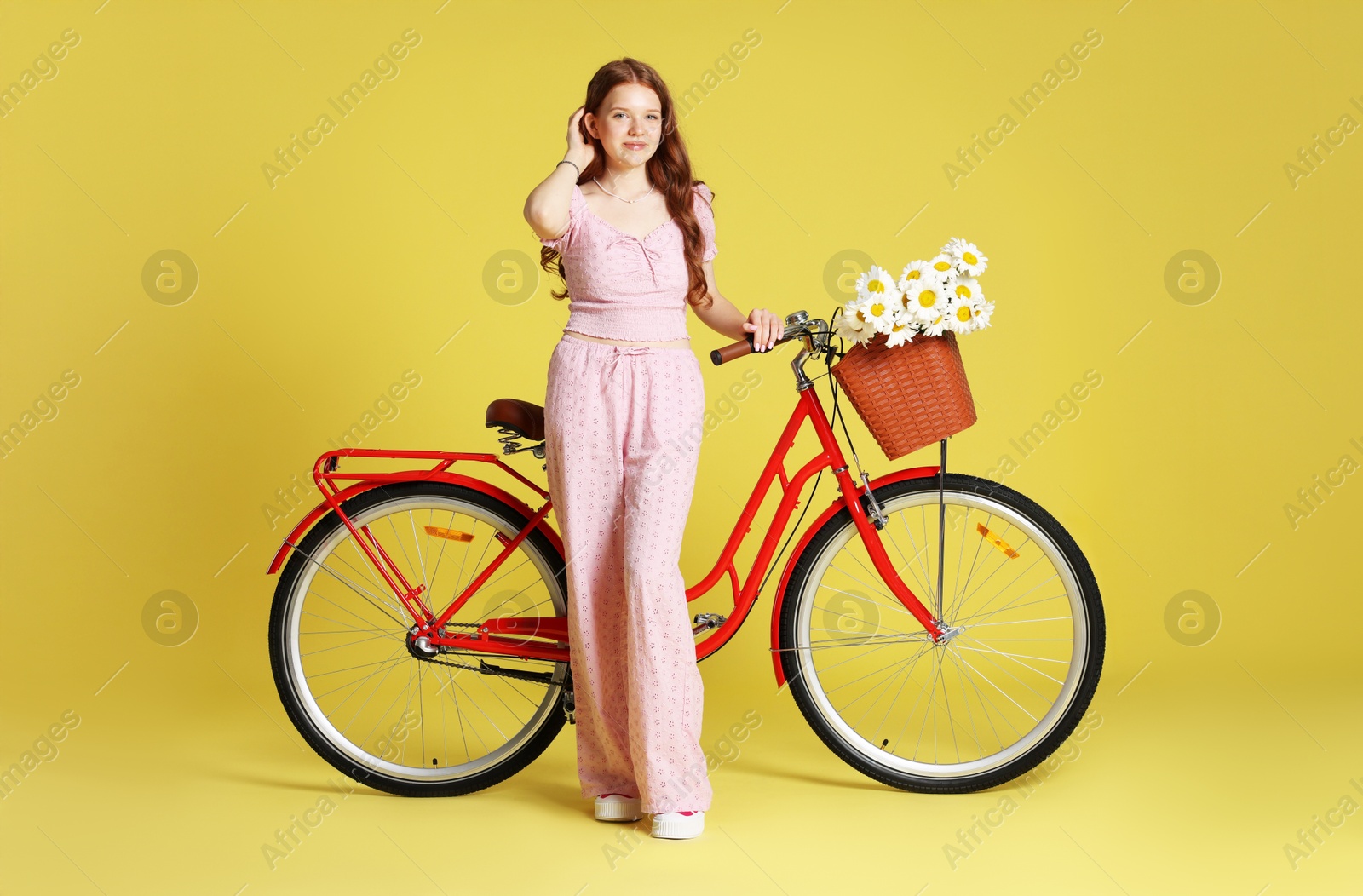 Beautiful teenage girl and bicycle with basket of flowers against light green background Photo of Beautiful teenage girl and bicycle with basket of flowers against light green background