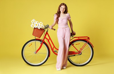 Photo of Smiling teenage girl and bicycle with basket of flowers against light green background