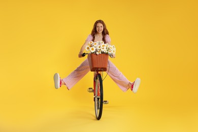 Photo of Smiling teenage girl riding bicycle with basket of flowers against yellow background