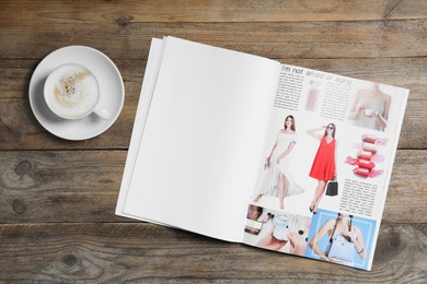 Photo of Open magazine and cup of coffee on wooden table, top view. Mockup for design
