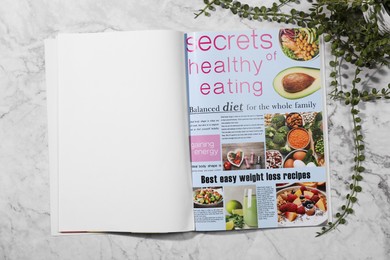 Photo of Open magazine and plant on white marble background, top view. Mockup for design