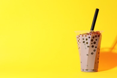 Photo of Tasty milk bubble tea in glass on yellow background, space for text