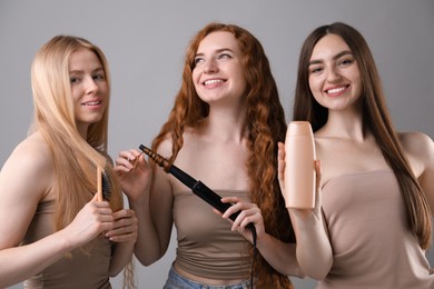Photo of Beautiful women with different hair colors holding curling iron, shampoo and brush on grey background