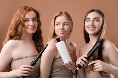 Photo of Beautiful women with different hair colors holding curling iron, shampoo and straightener on dark beige background