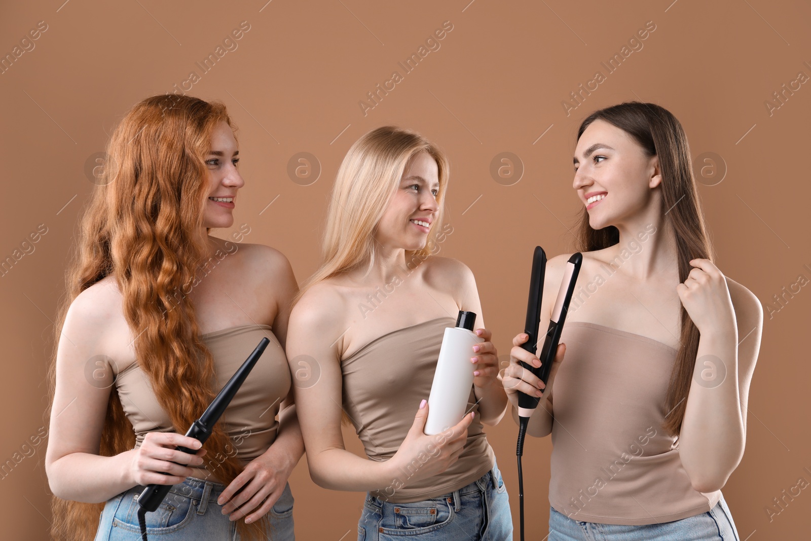 Beautiful women with different hair colors holding curling iron, shampoo and straightener on dark beige background Photo of Beautiful women with different hair colors holding curling iron, shampoo and straightener on dark beige background