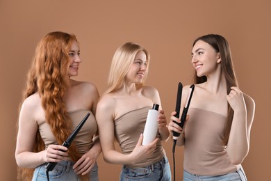 Photo of Beautiful women with different hair colors holding curling iron, shampoo and straightener on dark beige background
