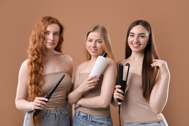 Photo of Beautiful women with different hair colors holding curling iron, shampoo and straightener on dark beige background