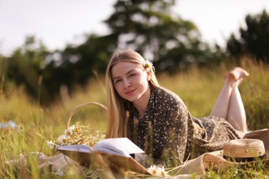 Photo of Beautiful woman with bouquet of wildflowers reading book on blanket in meadow