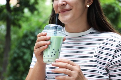 Photo of Woman with tasty milk bubble tea in plastic cup outdoors, closeup