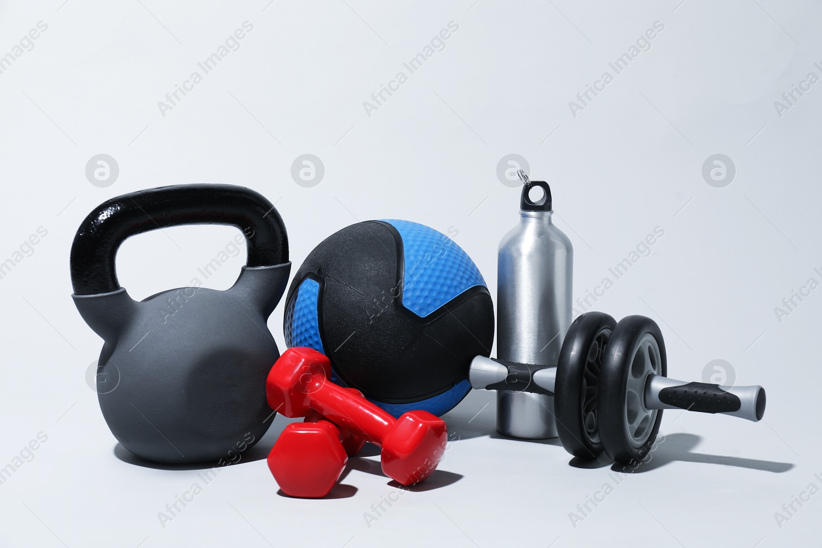 Medicine ball, kettlebell, water bottle, ab wheel and dumbbells on light grey background Photo of Medicine ball, kettlebell, water bottle, ab wheel and dumbbells on light grey background
