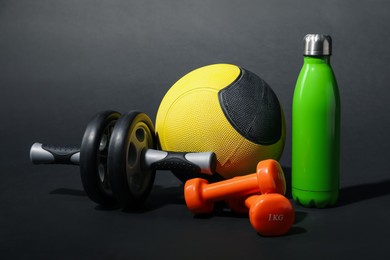 Photo of Medicine ball, dumbbells, ab wheel and water bottle on black background