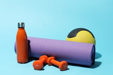 Photo of Medicine ball, fitness mat, water bottle and dumbbells on light blue background