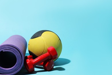 Photo of Medicine ball, fitness mat and dumbbells on light blue background. Space for text