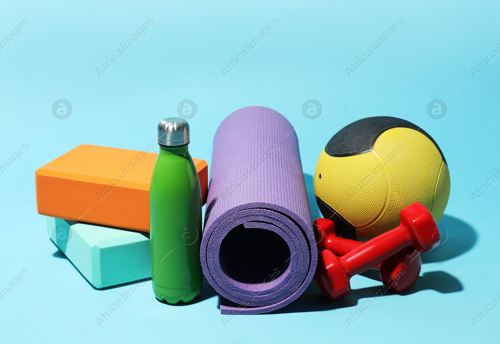 Medicine ball, foam blocks, fitness mat, water bottle and dumbbells on light blue background Photo of Medicine ball, foam blocks, fitness mat, water bottle and dumbbells on light blue background