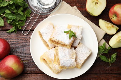 Photo of Pieces of tasty apple strudel with powdered sugar, mint and fruits on wooden table, flat lay