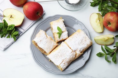 Photo of Pieces of tasty apple strudel with powdered sugar, mint and fruits on white marble table, flat lay