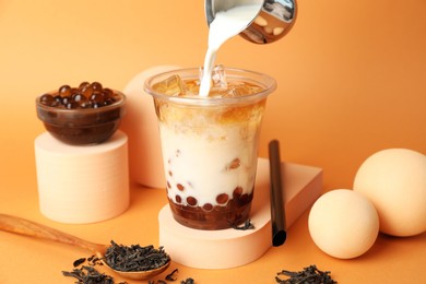 Photo of Pouring milk into bubble tea on orange background, closeup