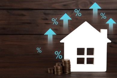 Image of Increase in real estate value. House model and coins on wooden background. Growing price represented by arrows and percent signs