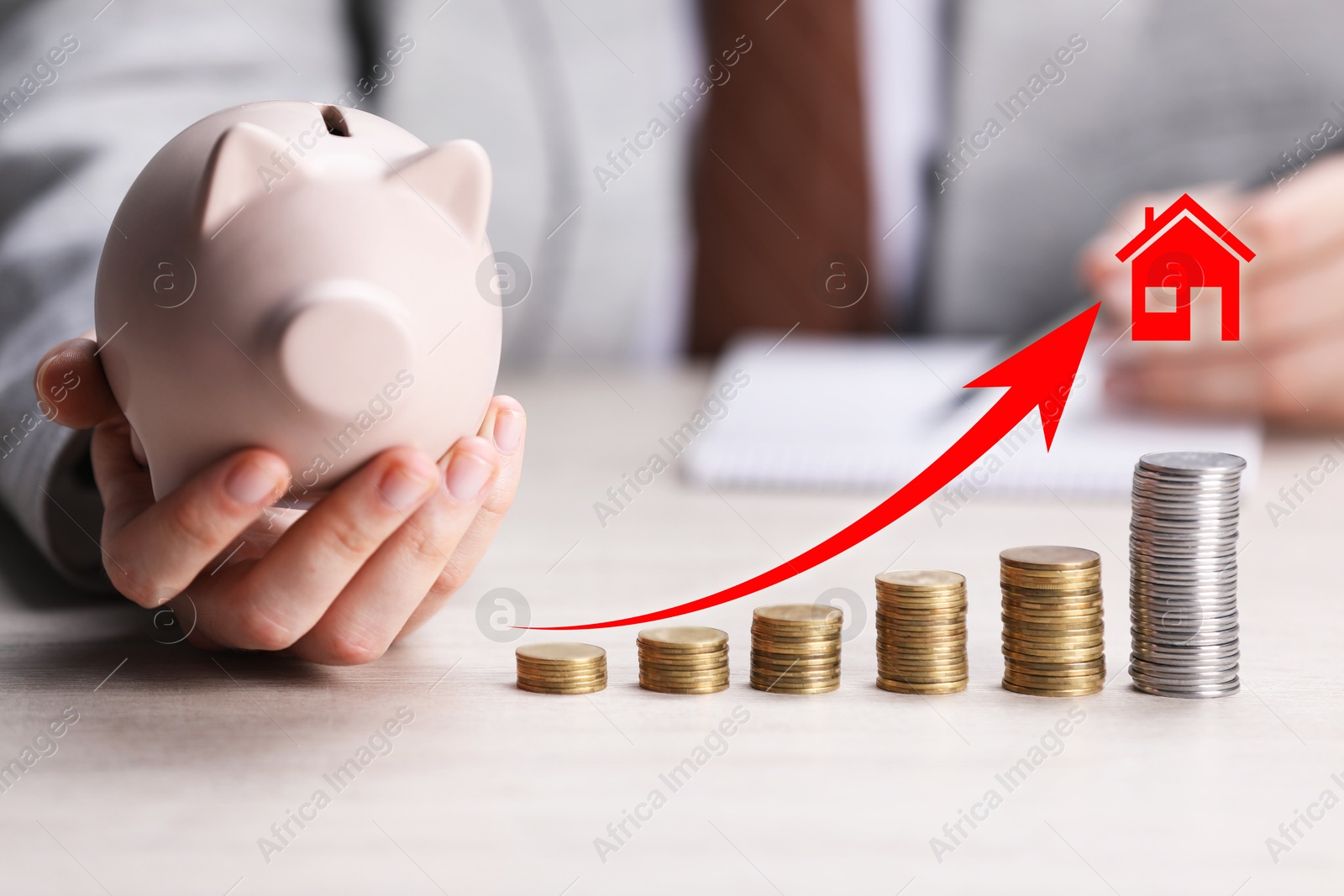 Increase in real estate value. Arrow and house icon above stacked coins. Man holding piggy bank at table, closeup Image of Increase in real estate value. Arrow and house icon above stacked coins. Man holding piggy bank at table, closeup