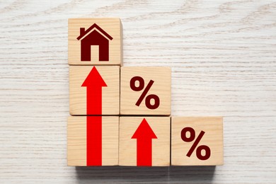 Image of Increase in real estate value. Cubes with house icon, arrows and percent signs on white table, top view