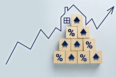 Image of Increase in real estate value. Arrow with house shape above cubes with arrows and percent signs on white table, top view