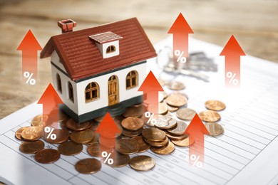 Image of Increase in real estate value. House model and coins on table. Growing price represented by arrows and percent signs
