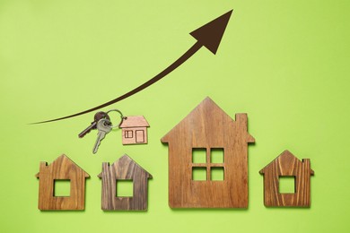 Image of Increase in real estate value. House models and key on light green background, top view. Growing price represented by arrow