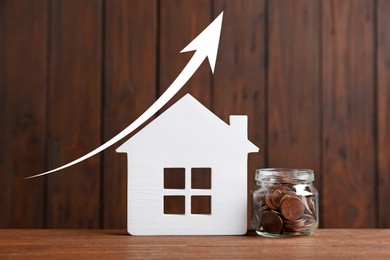 Image of Increase in real estate value. House model and jar of coins on wooden background. Growing price represented by arrow