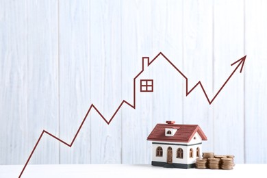 Image of Increase in real estate value. House model and coins on table. Growing price represented by arrow