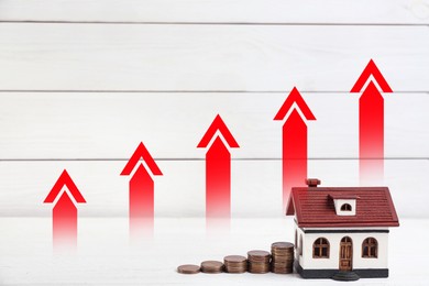 Image of Increase in real estate value. House model and coins on table. Growing price represented by arrows