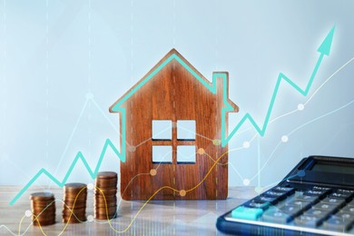 Image of Increase in real estate value. House model, coins and calculator on table. Growing price represented by graph and arrow