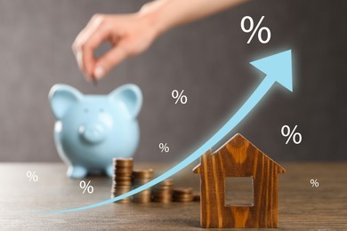 Image of Increase in real estate value. Arrow with percent signs above house model. Woman putting coin into piggy bank, selective focus
