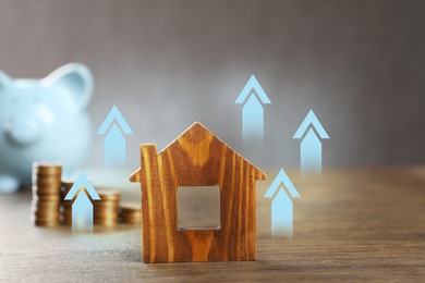 Image of Increase in real estate value. House model and coins on wooden table. Growing price represented by arrows