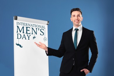 Image of International Men's Day card. Happy man pointing at board against blue background