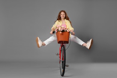 Photo of Smiling teenage girl riding bicycle with basket of flowers against grey background
