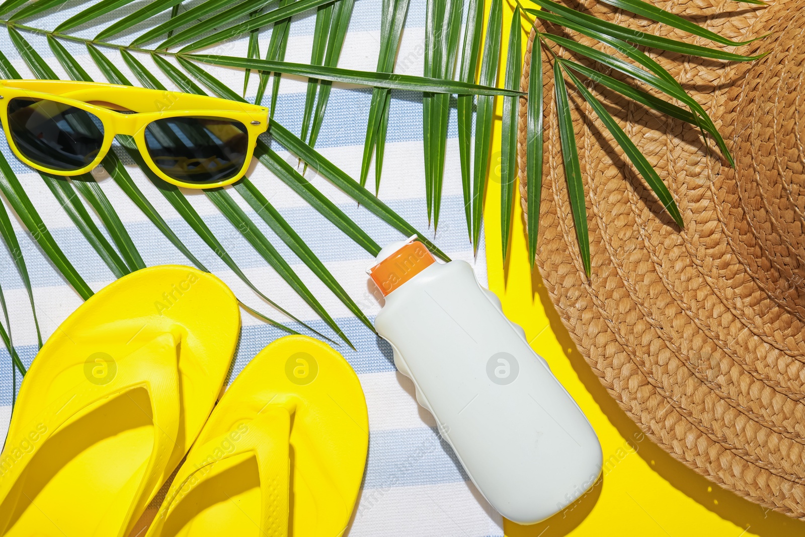 Beach towel, straw hat, flip flops, sunscreen product, sunglasses and palm leaf on yellow background, flat lay Photo of Beach towel, straw hat, flip flops, sunscreen product, sunglasses and palm leaf on yellow background, flat lay