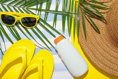 Photo of Beach towel, straw hat, flip flops, sunscreen product, sunglasses and palm leaf on yellow background, flat lay
