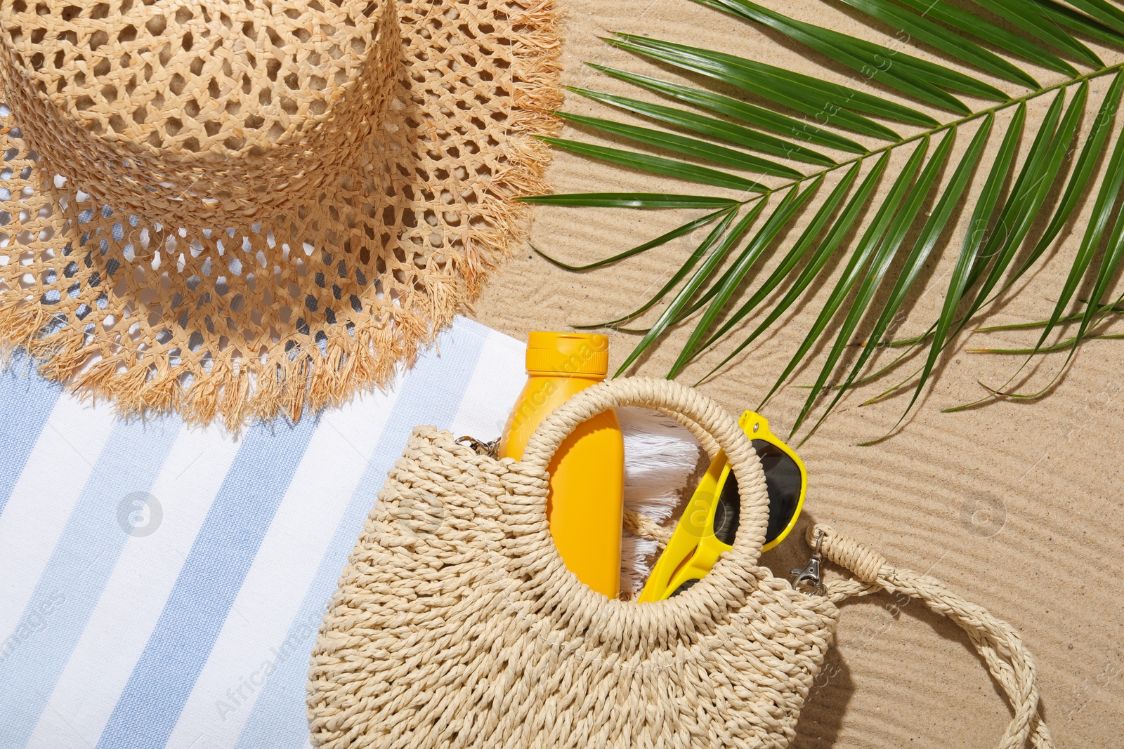 Beach towel, straw hat, bag, sunscreen product, sunglasses and palm leaf on sand outdoors, flat lay Photo of Beach towel, straw hat, bag, sunscreen product, sunglasses and palm leaf on sand outdoors, flat lay