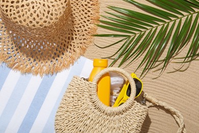 Photo of Beach towel, straw hat, bag, sunscreen product, sunglasses and palm leaf on sand outdoors, flat lay