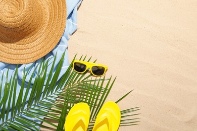 Photo of Beach towel, straw hat, sunglasses, flip flops and palm leaves on sand outdoors, flat lay. Space for text