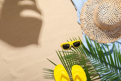 Photo of Beach towel, straw hat, sunglasses, flip flops and palm leaves on sand outdoors, flat lay. Space for text