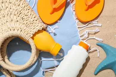 Photo of Beach towel, sunscreen products, flip flops, wicker bag and sea star on sand outdoors, flat lay