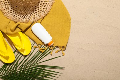 Photo of Beach towel, straw hat, flip flops, sunscreen product and palm leaf on sand outdoors, flat lay. Space for text