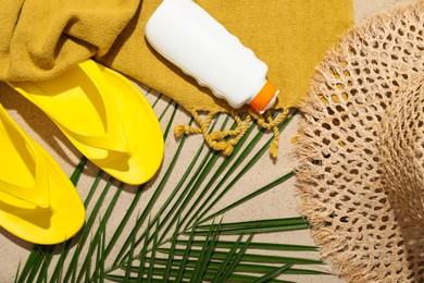 Photo of Beach towel, straw hat, flip flops, sunscreen product and palm leaf on sand outdoors, flat lay