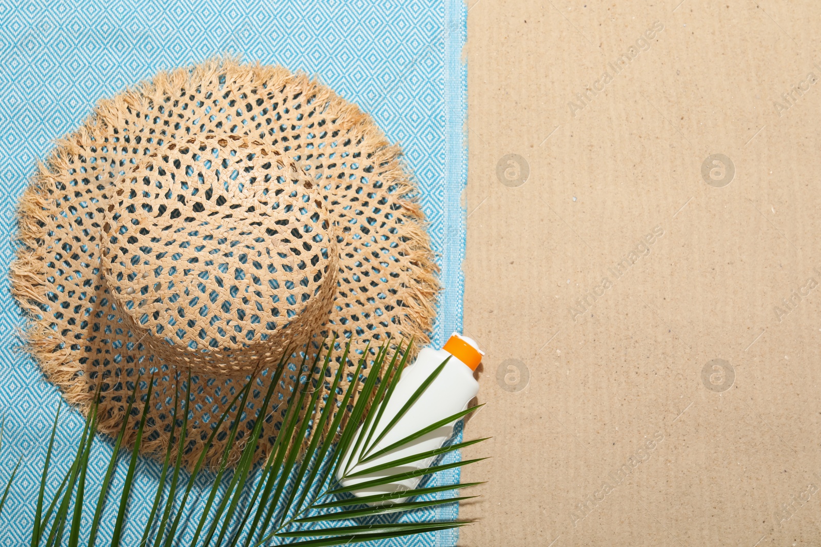 Beach towel, straw hat, sunscreen product and palm leaf on sand outdoors, flat lay. Space for text Photo of Beach towel, straw hat, sunscreen product and palm leaf on sand outdoors, flat lay. Space for text