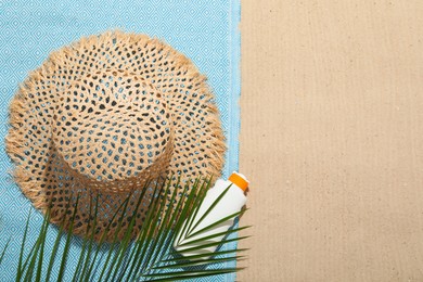 Photo of Beach towel, straw hat, sunscreen product and palm leaf on sand outdoors, flat lay. Space for text