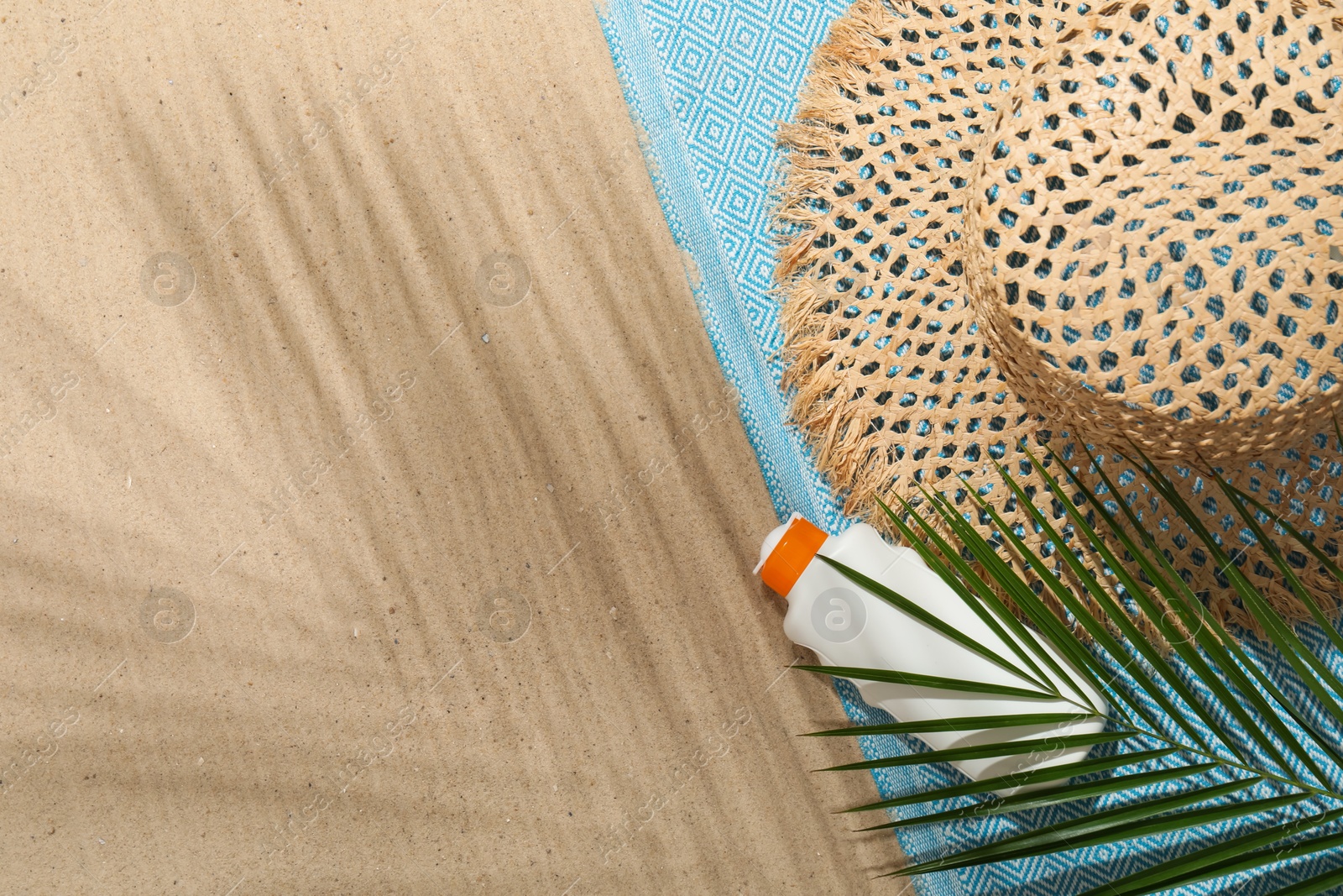 Beach towel, straw hat, sunscreen product and palm leaf on sand outdoors, flat lay. Space for text Photo of Beach towel, straw hat, sunscreen product and palm leaf on sand outdoors, flat lay. Space for text