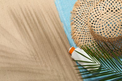 Photo of Beach towel, straw hat, sunscreen product and palm leaf on sand outdoors, flat lay. Space for text