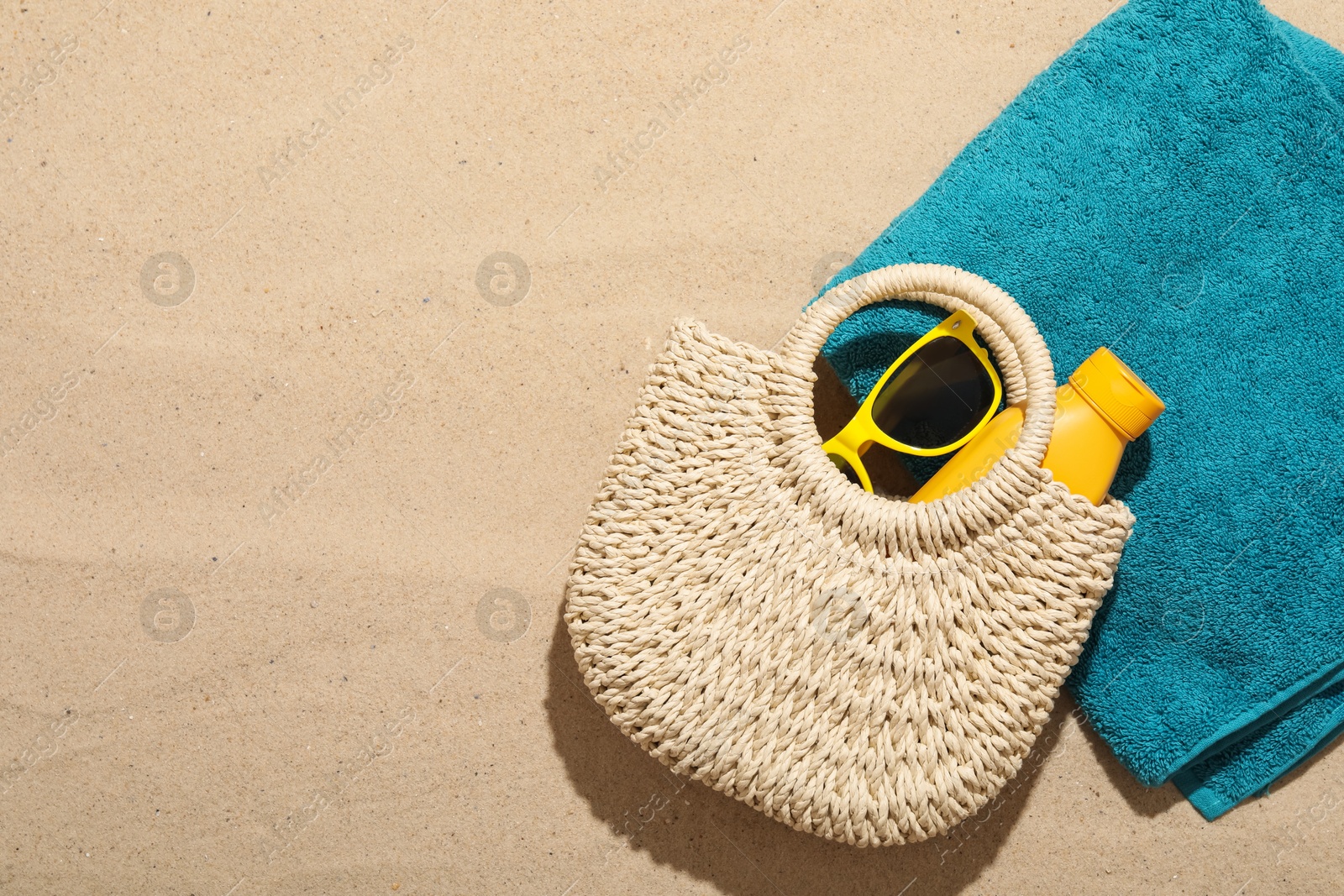 Photo of Beach towel, straw bag, sunscreen product and sunglasses on sand outdoors, flat lay. Space for text