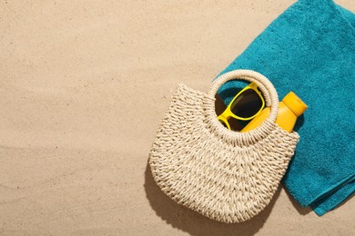 Photo of Beach towel, straw bag, sunscreen product and sunglasses on sand outdoors, flat lay. Space for text